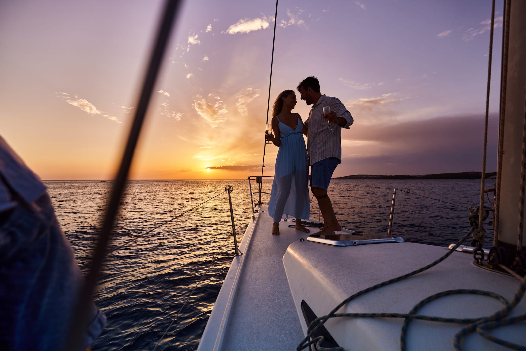 Couple enjoying sunset on a sailing boat with glass of wine in hand.